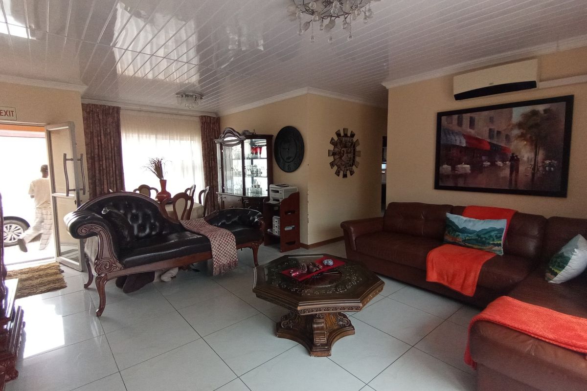 Spacious living room featuring large format floor tiles, a glossy panelled ceiling, and a wall-mounted air conditioning unit.
