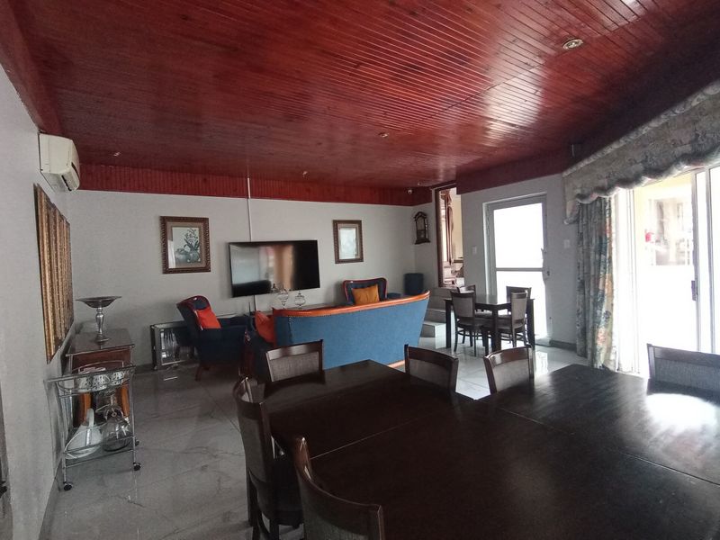 Spacious open-plan living and dining area featuring a distinctive timber-clad ceiling, tiled flooring, and direct access to the outdoor area via sliding glass doors.
