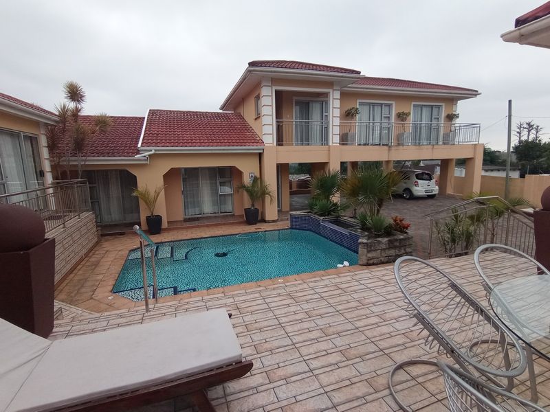 A multi-level residential exterior featuring a swimming pool, paved patio area, and a balcony overlooking the property grounds.