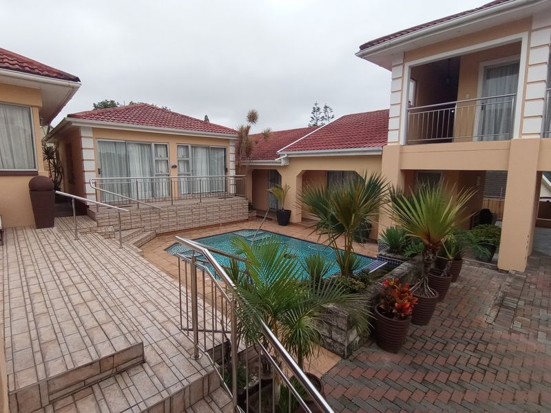 A well-maintained outdoor pool area featuring a tiled patio, brick paving, and stainless steel railings connecting multiple sections of the property.