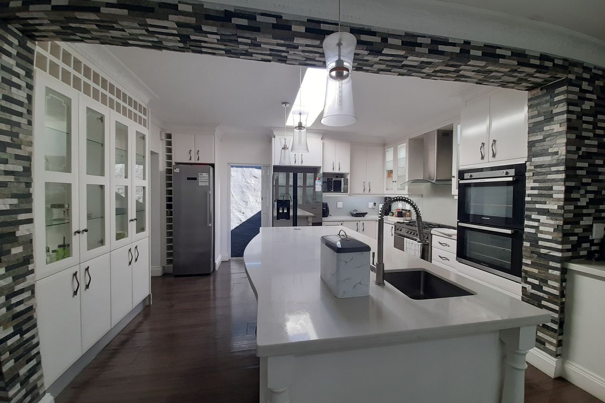 Spacious modern kitchen featuring a large central island, stone countertops, double wall oven, ample cabinetry, and a skylight for natural illumination.
