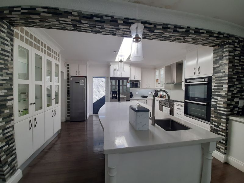 Spacious modern kitchen featuring a large central island, stone countertops, double wall oven, ample cabinetry, and a skylight for natural illumination.