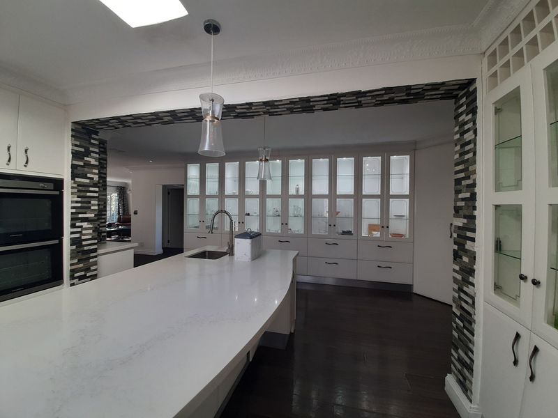 Spacious kitchen featuring a large island with stone countertops, built-in double ovens, extensive glass-front cabinetry, and elegant pendant lighting.