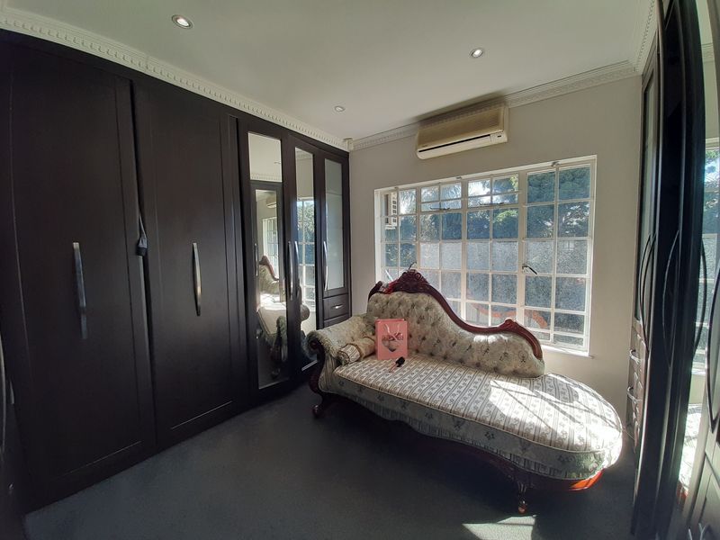 A bedroom featuring extensive dark wood built-in cupboards with mirrored panels, recessed lighting, crown molding, and a wall-mounted air conditioning unit.