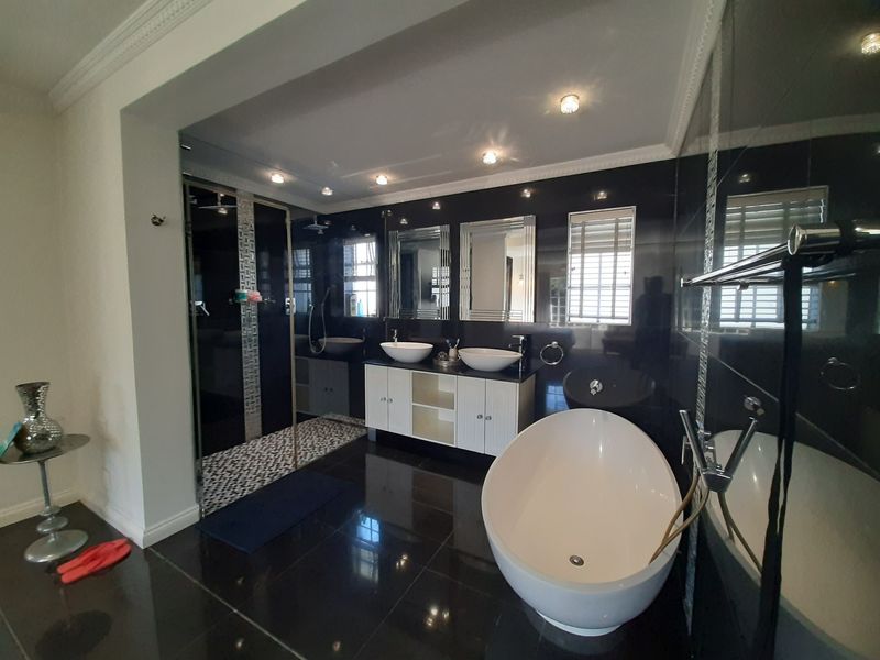 Modern bathroom featuring a double vanity, a sleek freestanding bathtub, and a spacious walk-in shower with high-contrast black tiling and recessed lighting.