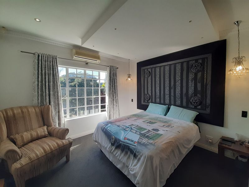 A well-lit bedroom featuring a recessed ceiling with downlights, wall-mounted air conditioning, and large windows providing natural light.