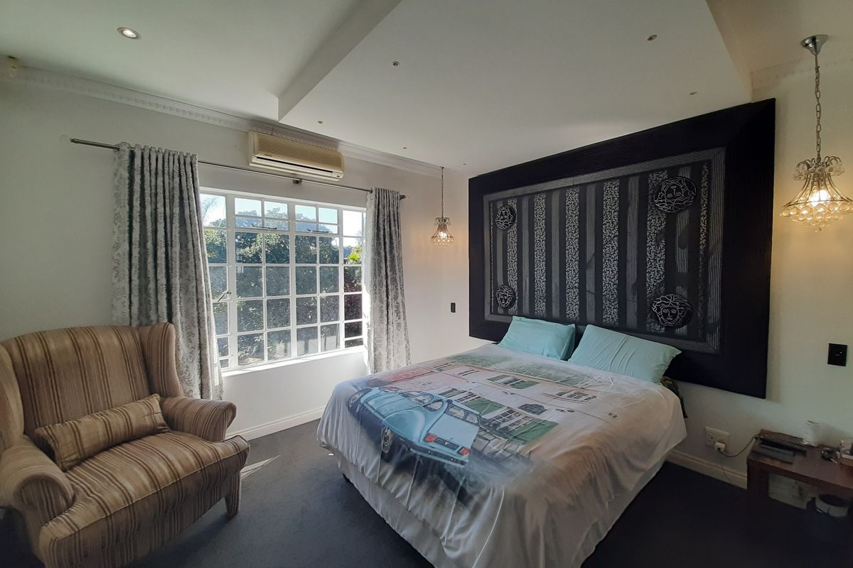A well-lit bedroom featuring a recessed ceiling with downlights, wall-mounted air conditioning, and large windows providing natural light.