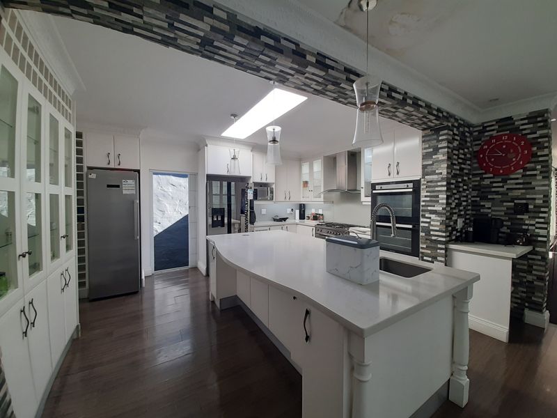 Spacious kitchen featuring a large central island, stone countertops, built-in double oven, gas cooktop, and ample cabinetry with a stone veneer feature wall.