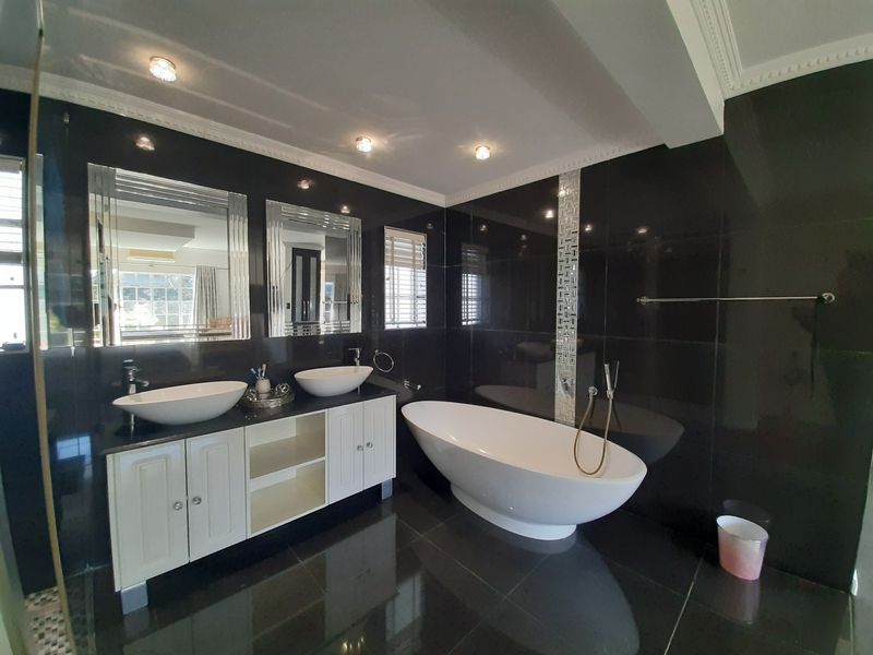 Modern bathroom featuring a double vanity with vessel sinks, a sleek freestanding bathtub, and dark polished wall and floor tiles.