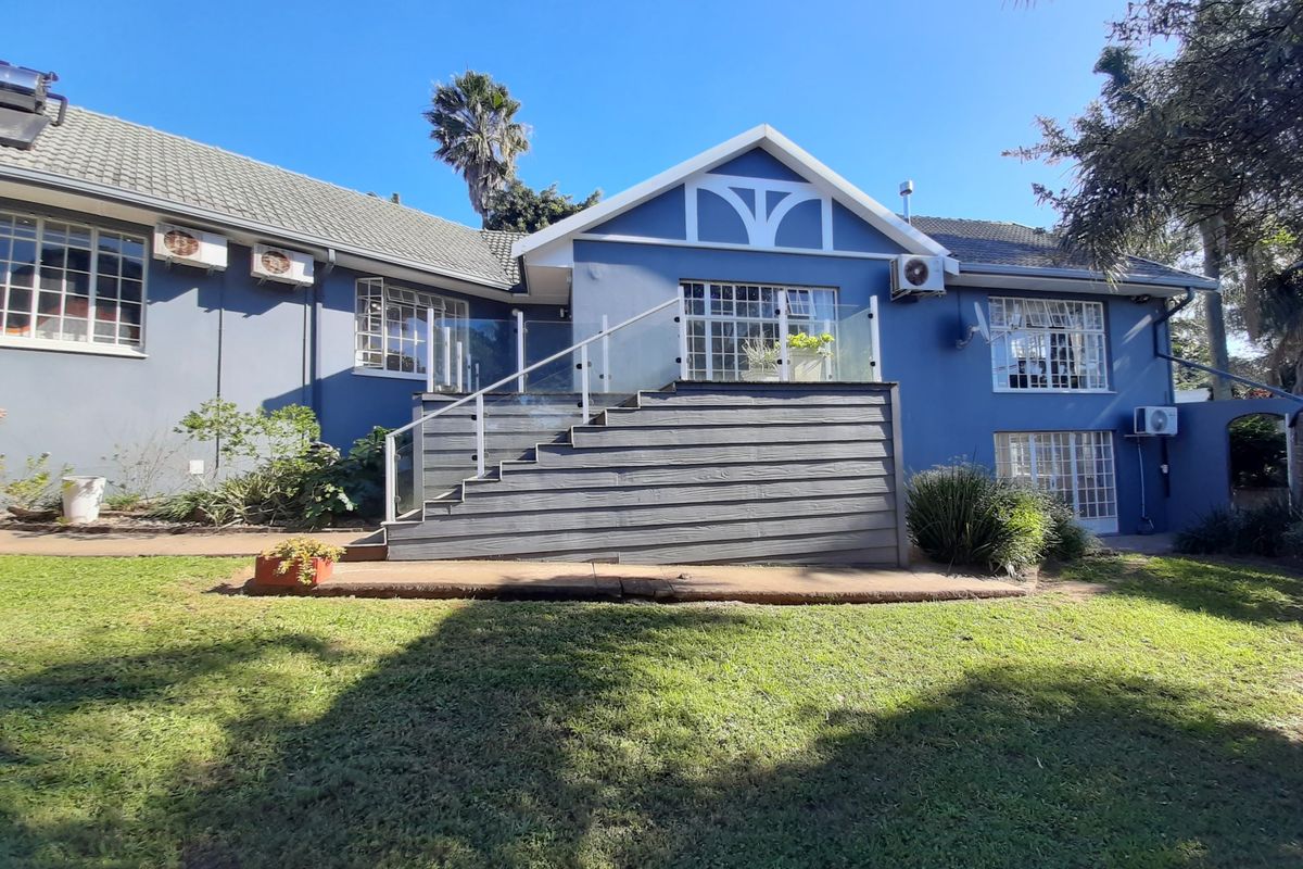 Rear view of the house featuring a blue facade, a raised timber deck with glass balustrades, and a concrete patio overlooking the garden.