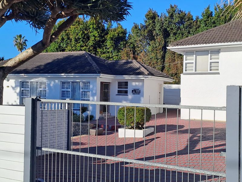 Front view of a residential property featuring a paved driveway, tiled roof, and secure metal gate entrance.