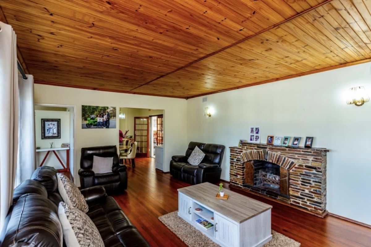 Spacious living room featuring a warm timber ceiling, polished hardwood floors, and a classic stone fireplace as a central focal point.