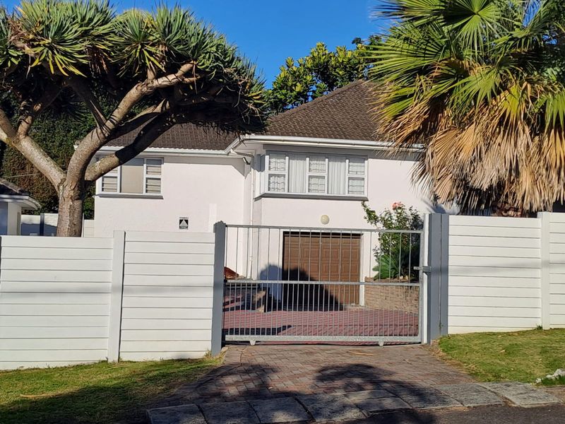 Front view of a residential property featuring a paved driveway, secure metal gate, garage, and well-maintained boundary walls.