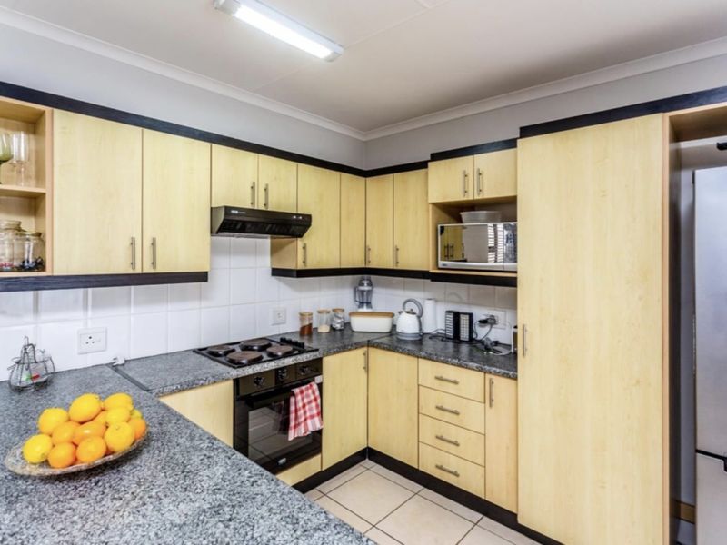 Functional kitchen featuring light wood cabinetry, granite countertops, built-in oven, hob, extractor fan, and tiled flooring.
