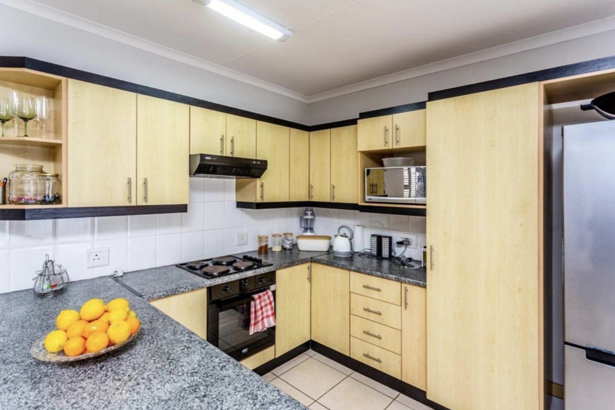 Functional kitchen featuring light wood cabinetry, granite countertops, built-in oven, hob, extractor fan, and tiled flooring.