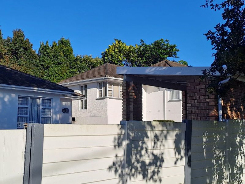 A view of the front exterior of the house featuring white rendered walls, tiled roofing, and a secure precast concrete boundary wall.