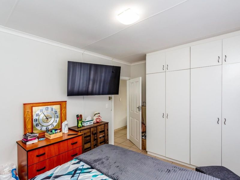A functional bedroom featuring built-in white cupboards, tiled flooring, and a coved ceiling, providing ample storage and a neutral base.