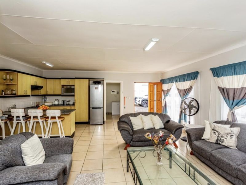 Open-plan living area featuring a functional kitchen with built-in cabinetry, island seating, and tiled flooring, seamlessly connected to the lounge space.