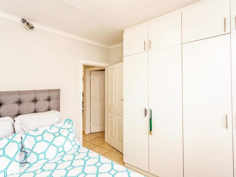 A well-maintained bedroom featuring ample built-in cupboard storage, neutral tiled flooring, and clean finishes, providing a functional and comfortable living space.