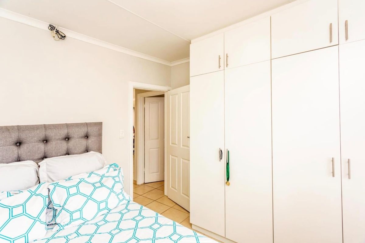 A well-maintained bedroom featuring ample built-in cupboard storage, neutral tiled flooring, and clean finishes, providing a functional and comfortable living space.