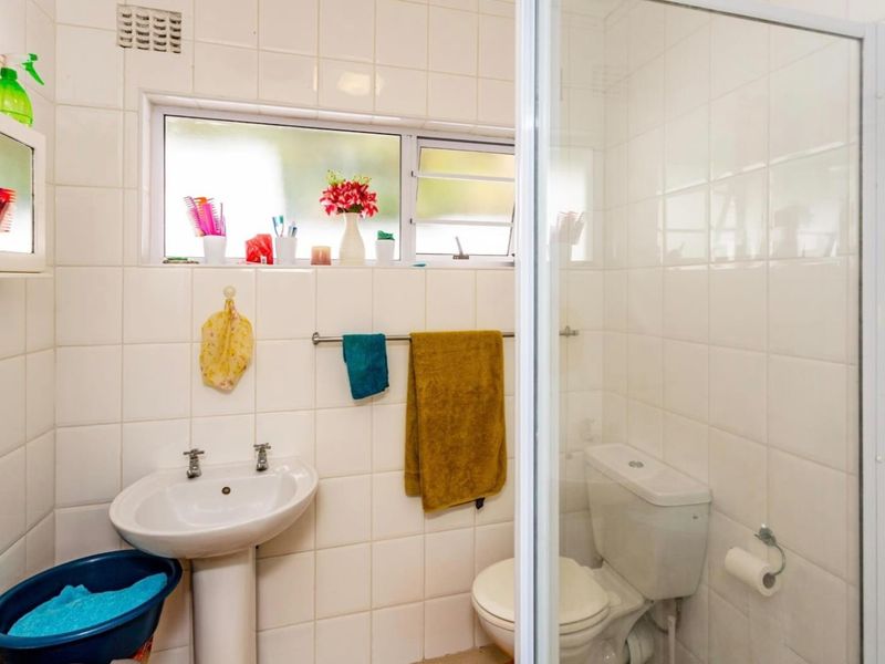 A compact bathroom featuring a pedestal basin, toilet, and shower enclosure with white wall tiling and a louvered window for ventilation.