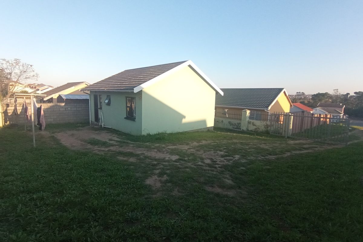 Rear view of a detached house featuring a tiled roof, perimeter wall, and metal fencing, set within a large, partially grassed yard.