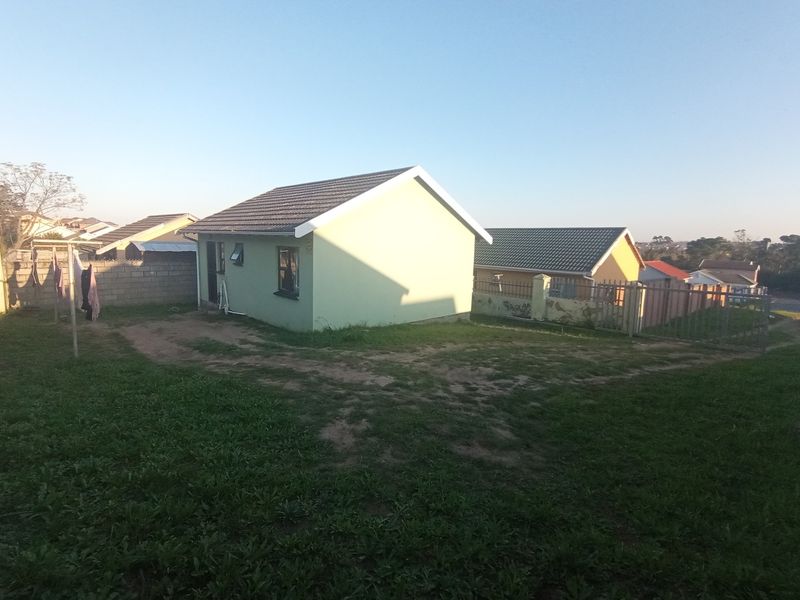 Rear view of a detached house featuring a tiled roof, perimeter wall, and metal fencing, set within a large, partially grassed yard.
