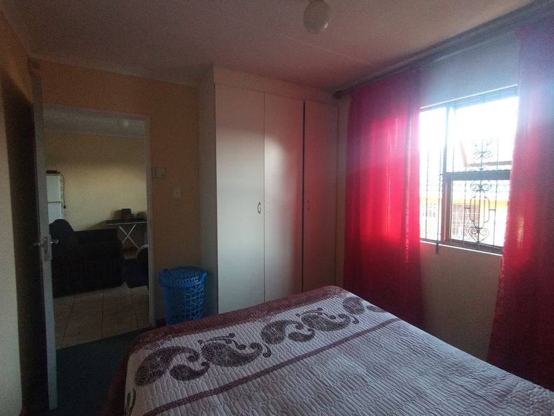 A functional bedroom featuring a built-in wardrobe and a window fitted with a security gate, offering a view into the adjacent living area.