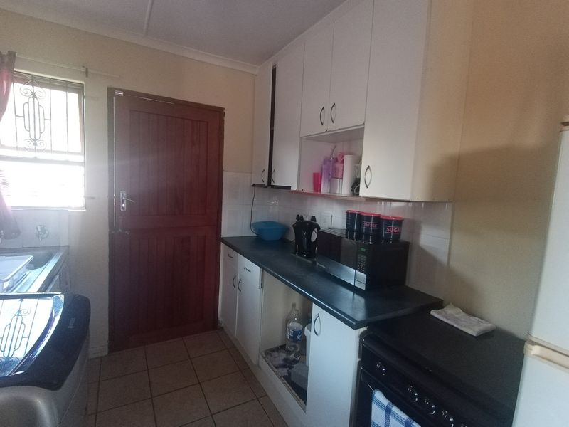 A functional kitchen featuring built-in cabinetry, laminate countertops, tiled splashbacks, and tiled flooring with direct access to an exterior door.
