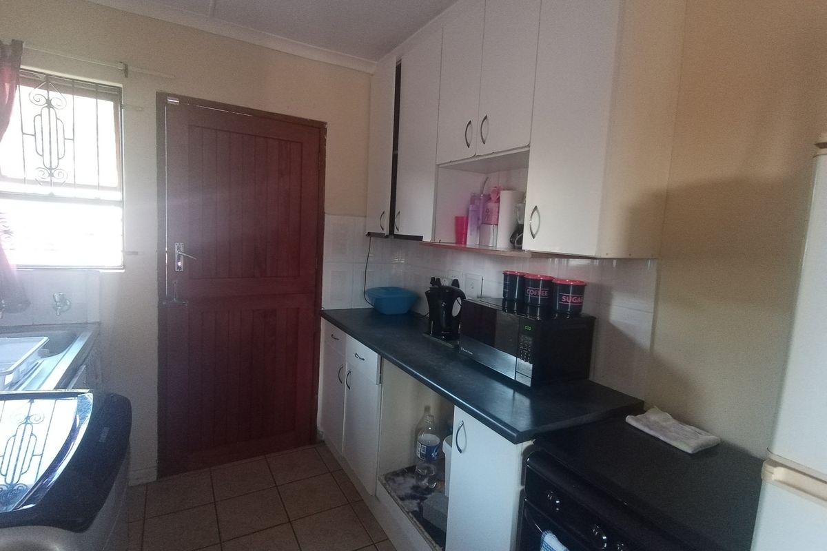 A functional kitchen featuring built-in cabinetry, laminate countertops, tiled splashbacks, and tiled flooring with direct access to an exterior door.