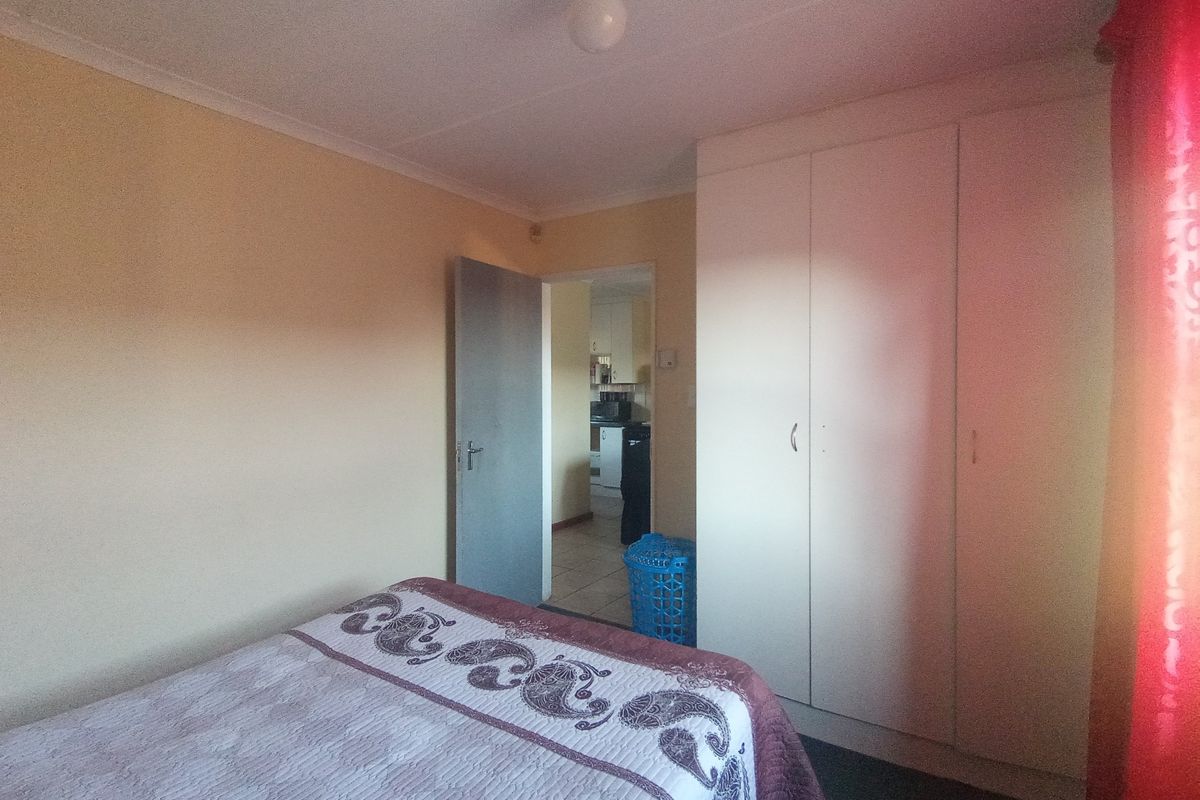 A bedroom featuring built-in cupboards and cove cornice detailing, with a doorway leading to an adjacent kitchen area.