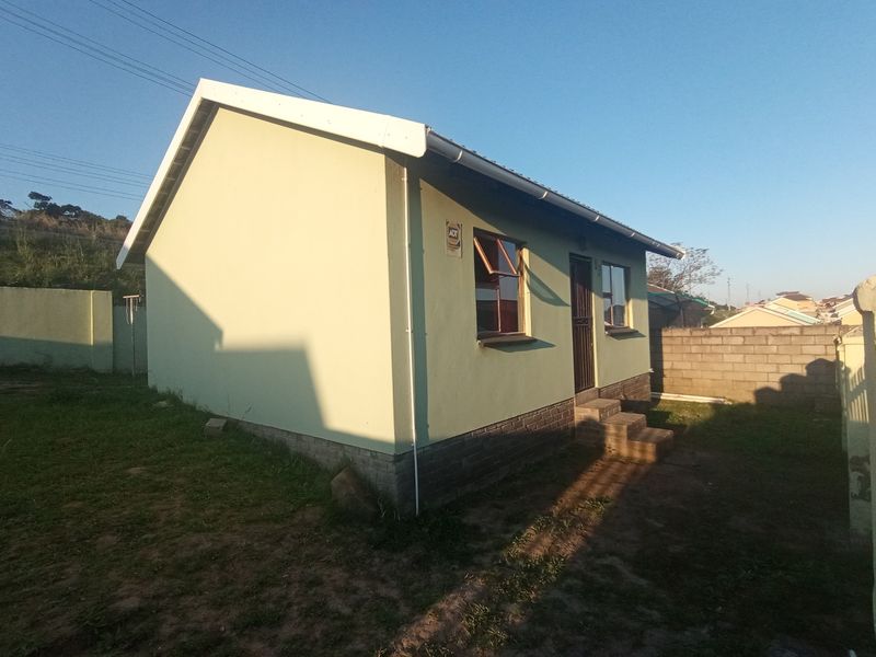 Rear view of a detached house featuring a brick plinth, security gate, and casement windows set within a fenced yard.