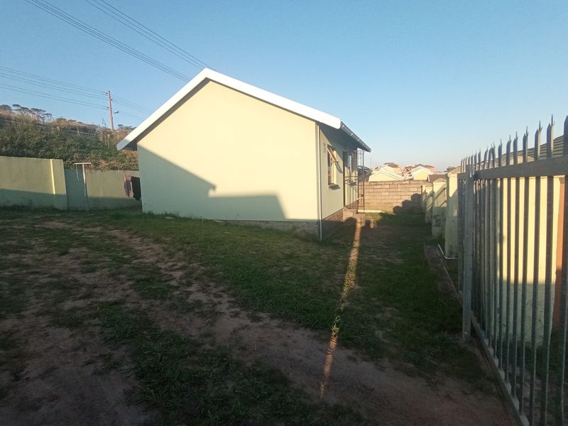 A view of the rear exterior of the house featuring a gable roof, perimeter wall, and metal security fencing.