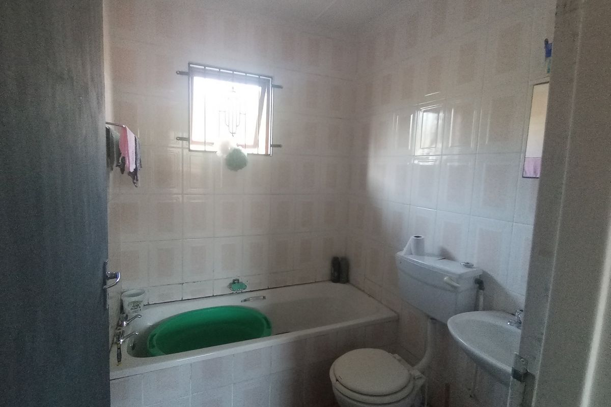 A functional bathroom featuring a bathtub, pedestal basin, and toilet with full-height wall tiling and a security-grille window.