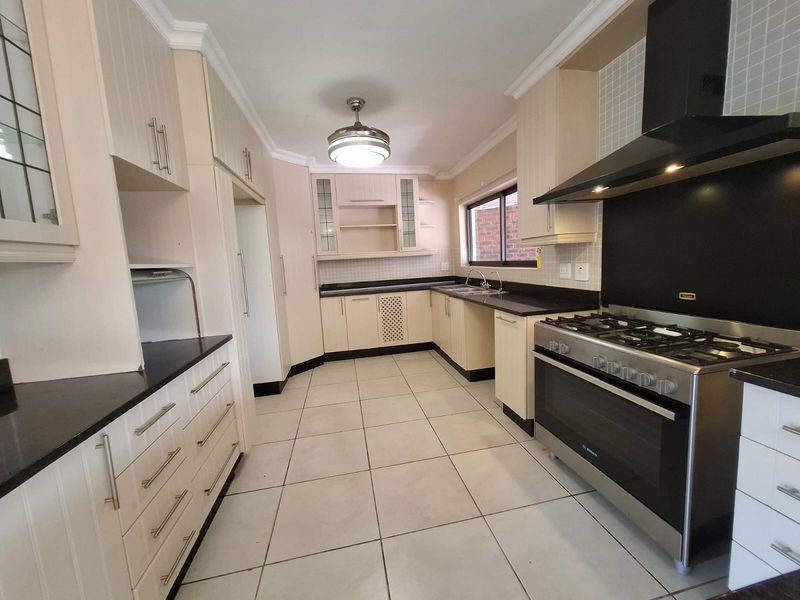 A clean, functional kitchen featuring ample built-in cabinetry, granite countertops, a gas stove with extractor fan, and tiled flooring.