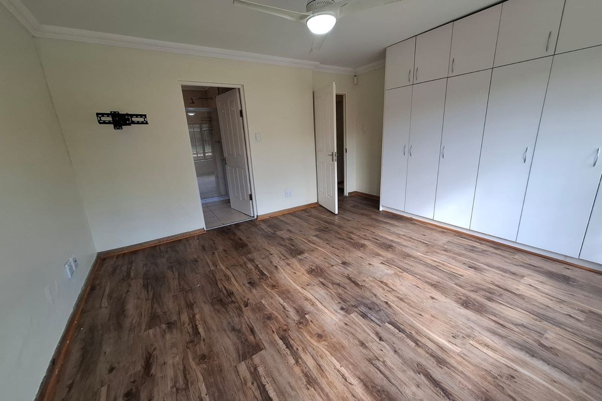 Spacious bedroom featuring wood-look laminate flooring, extensive built-in cupboards, a ceiling fan, and direct access to an en-suite bathroom.