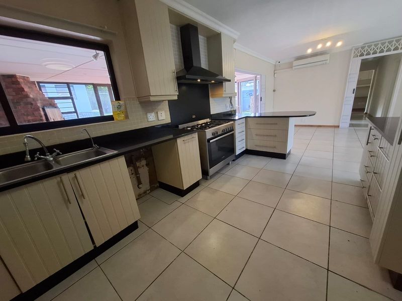 A functional kitchen featuring built-in cabinetry, a gas stove with extractor fan, and a breakfast bar, with tiled flooring throughout.
