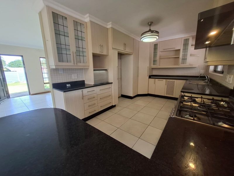 A spacious kitchen featuring light-toned built-in cabinetry, dark granite countertops, a gas hob with extractor, and tiled flooring, offering a functional layout.