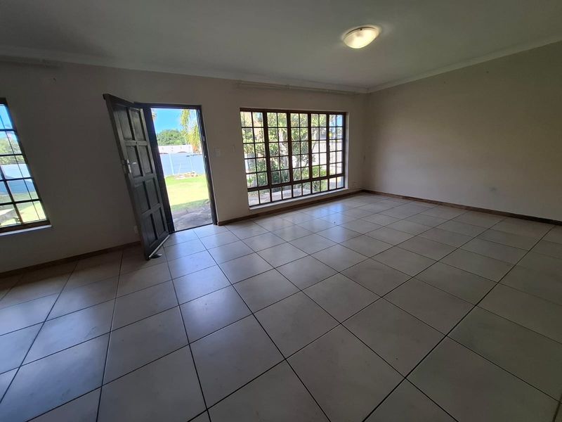 A spacious, empty living area featuring neutral tiled flooring, large multi-pane windows providing natural light, and direct access to the garden.