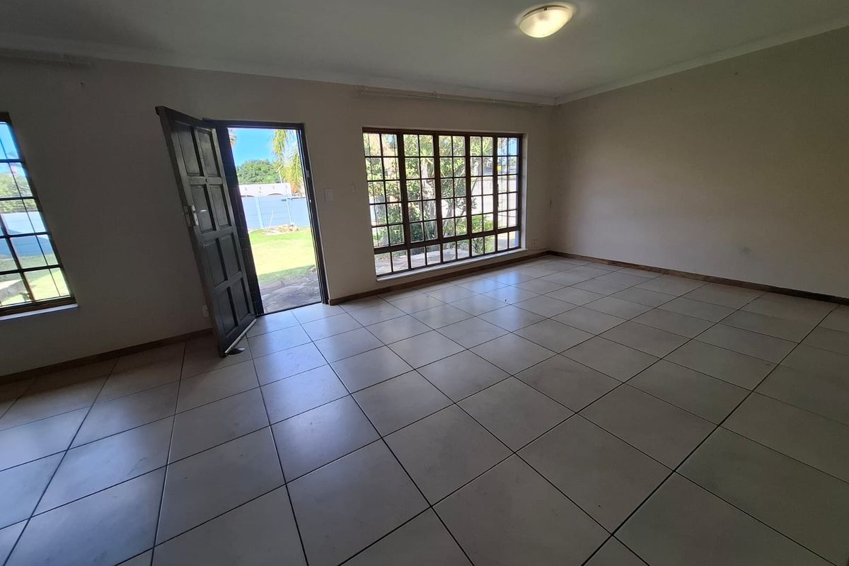 A spacious, empty living area featuring neutral tiled flooring, large multi-pane windows providing natural light, and direct access to the garden.