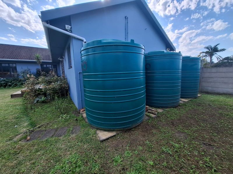 Rear exterior view of the property featuring three large water storage tanks installed alongside the building wall.