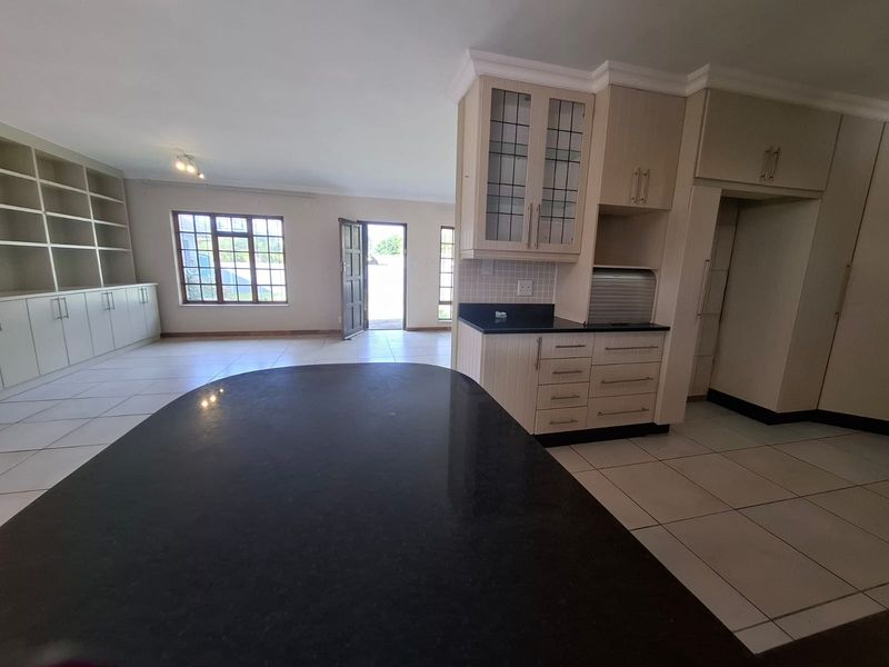 Spacious open-plan living and kitchen area featuring tiled flooring, extensive built-in cabinetry, granite countertops, and a large built-in shelving unit.