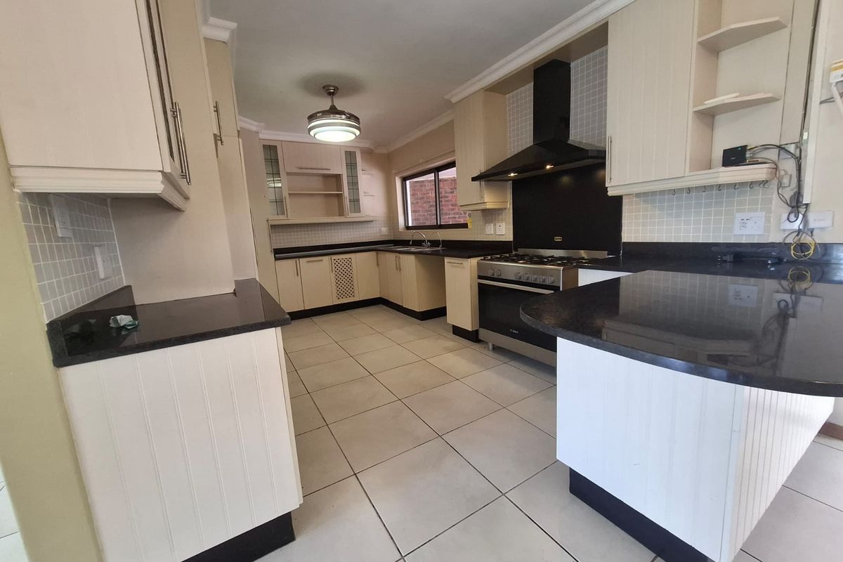 Spacious kitchen featuring granite countertops, ample built-in cabinetry, a gas stove with extractor fan, and tiled flooring throughout.