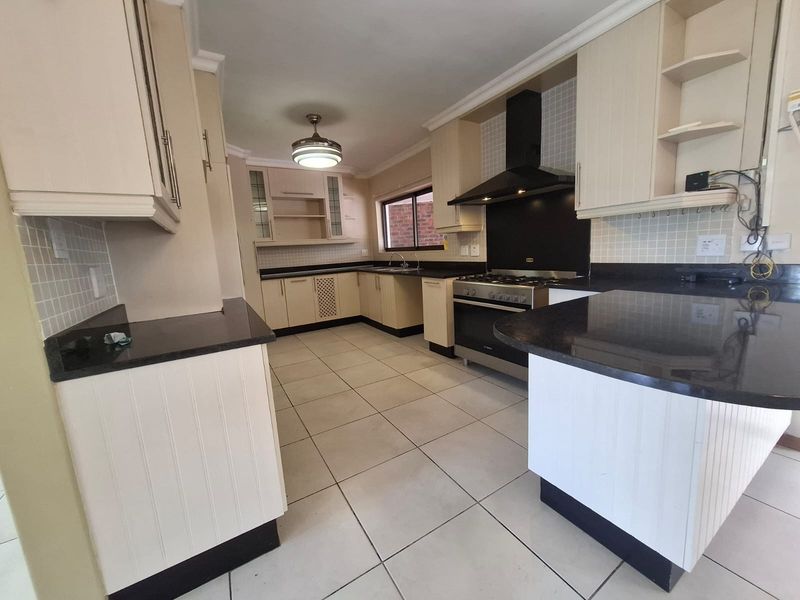 Spacious kitchen featuring granite countertops, ample built-in cabinetry, a gas stove with extractor fan, and tiled flooring throughout.