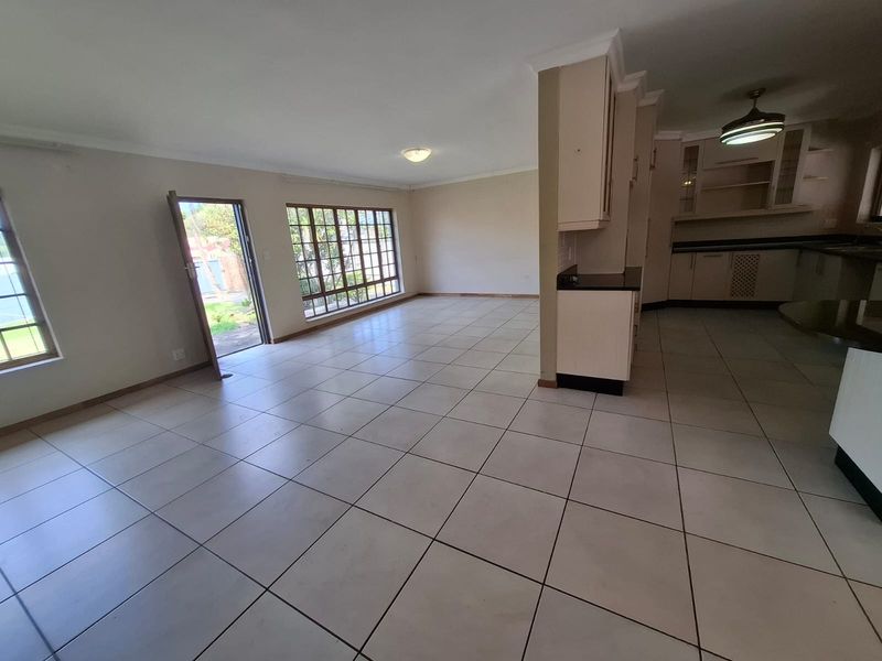 Spacious open-plan living area featuring tiled flooring, neutral walls, and an adjoining kitchen with built-in cabinetry and granite countertops.