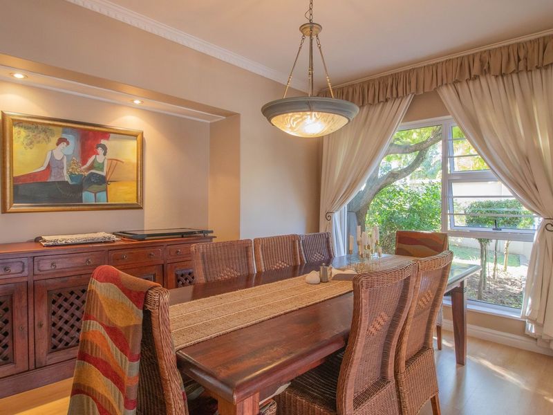 A well-lit dining room featuring laminate flooring, decorative ceiling cornices, and a large window providing natural light and garden views.