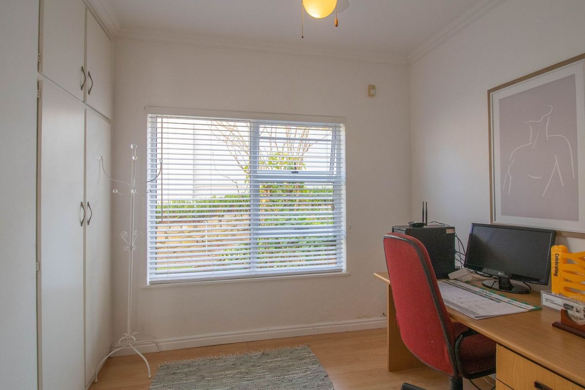 A functional bedroom featuring laminate flooring, built-in cupboards for storage, and a window fitted with venetian blinds.