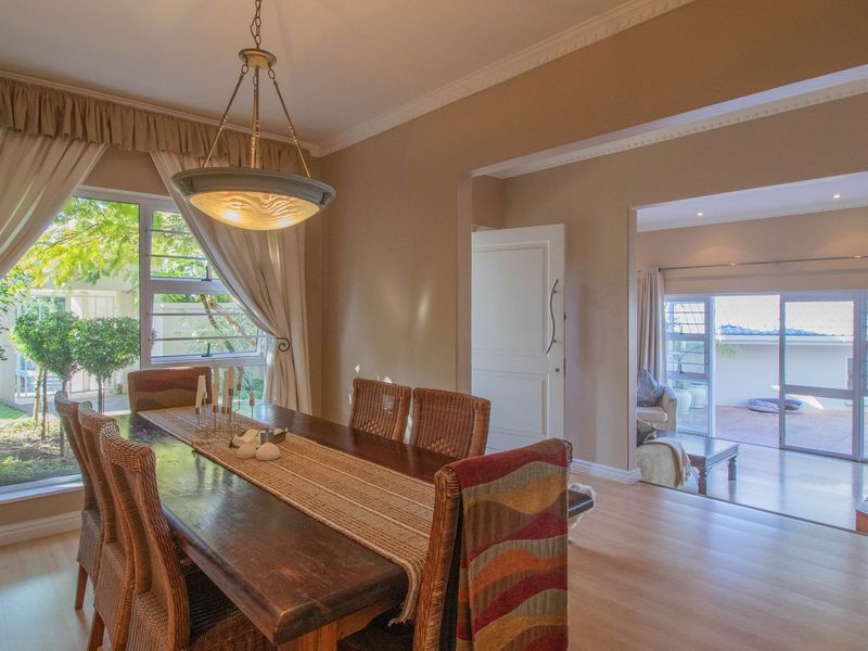 A bright dining room featuring laminate flooring, crown molding, and large windows overlooking the garden, with an open flow into the adjacent living area.