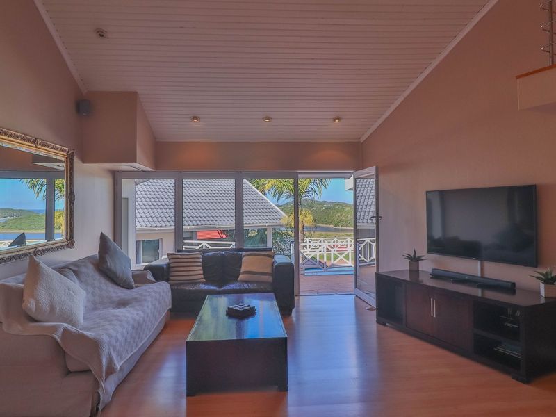 Spacious living room featuring vaulted timber ceilings, laminate flooring, and large glass doors opening to an outdoor balcony with scenic views.