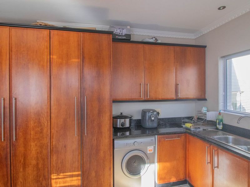 A functional scullery featuring wood-finish cabinetry, granite countertops, and a stainless steel double sink with a dedicated space for laundry appliances.